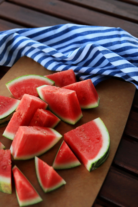 Numerous slices of watermelon on a wooden cutting board, next to a blue and white striped dish towel